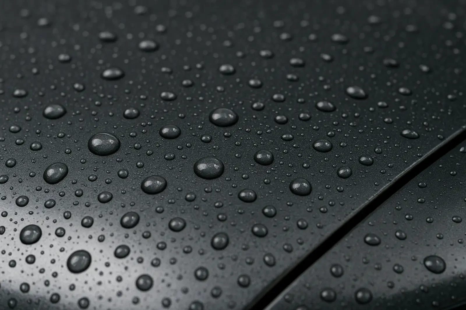 Wassertropfen auf einer glatten, schwarzen Oberfläche eines Fahrzeugs, die Licht reflektieren.