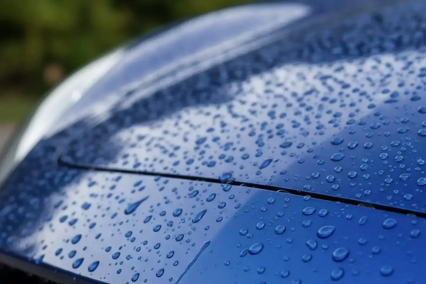 Nahaufnahme von Wassertropfen auf einer blauen Autolackoberfläche.