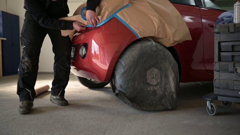Ein Mann bringt eine Schutzfolie an einem roten Auto an, während das Rad mit einer Abdeckung geschützt ist.
