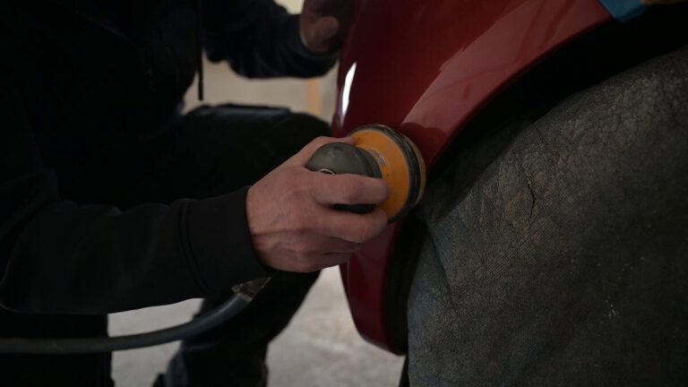 Eine Person verwendet eine Poliermaschine an einer roten Fahrzeugoberfläche während der Fahrzeugaufbereitung.