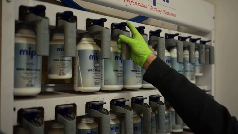 Hand greift nach einer Flasche mit Lack in einem professionellen Beschichtungssystem.