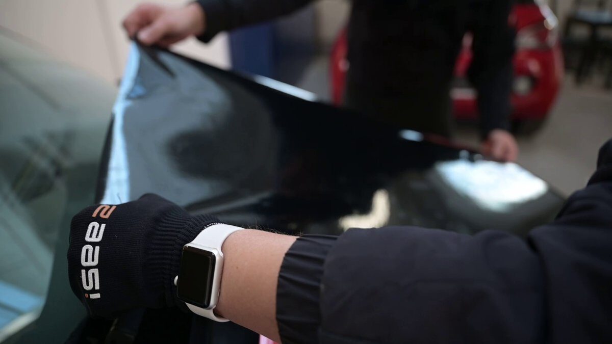 Person zieht eine schwarze Folie von der Motorhaube eines Fahrzeugs ab.