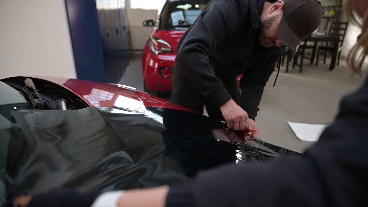Ein Mann, der eine schwarze Folie auf die Karosserie eines Fahrzeugs anbringt.