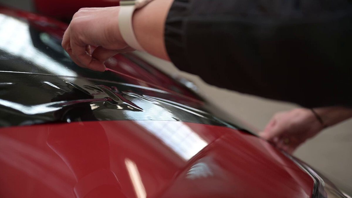 Eine Person, die eine schwarze Folie auf die Oberfläche eines roten Fahrzeugs anbringt.