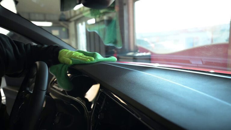 Eine Person reinigt das Armaturenbrett eines Autos mit einem grünen Tuch.