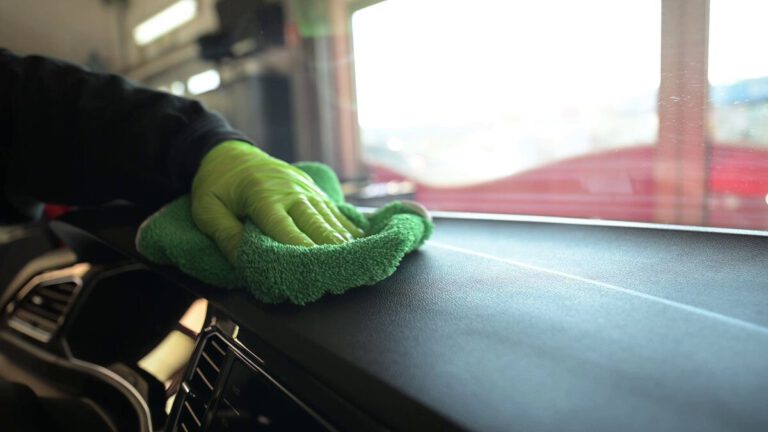 Eine Hand mit einem grünen Tuch reinigt das Armaturenbrett eines Fahrzeugs.