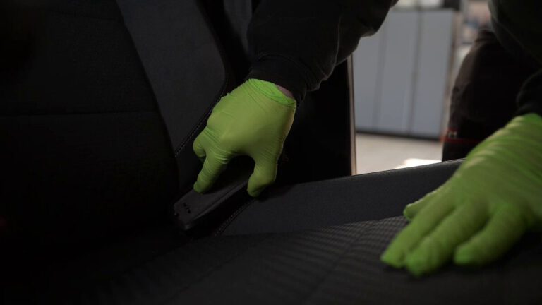 Person mit grünen Handschuhen reinigt den Autositz in einem Fahrzeug.