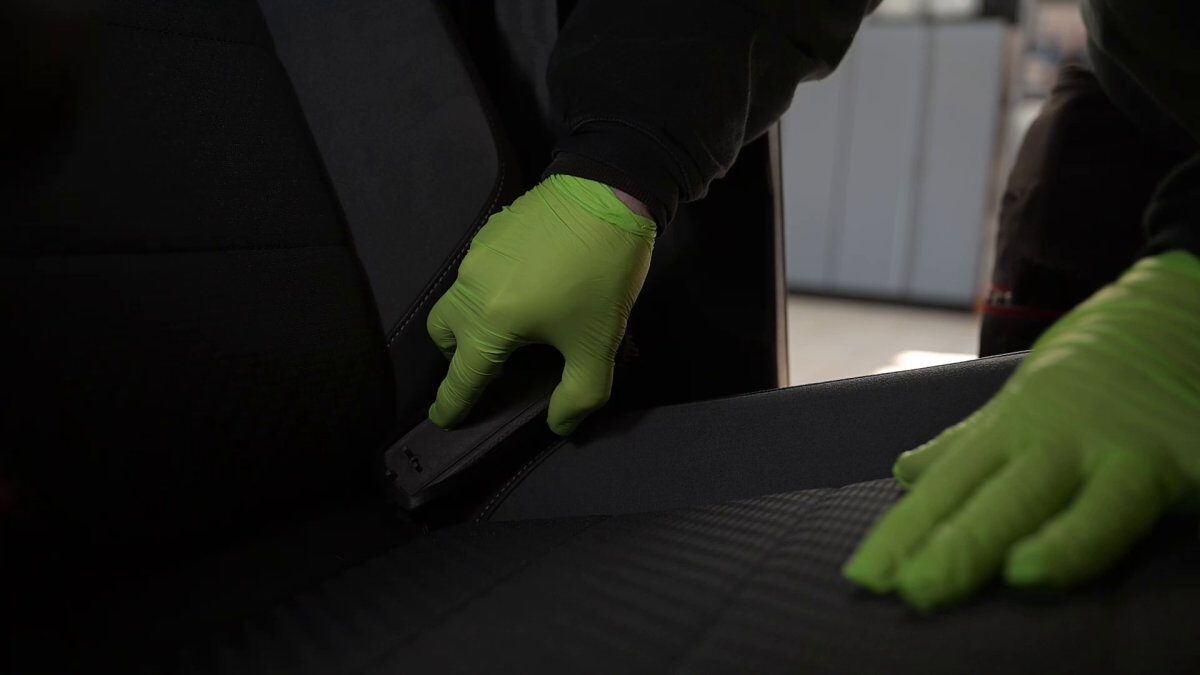 Person mit grünen Handschuhen reinigt den Autositz in einem Fahrzeug.