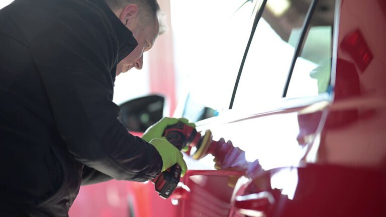 Ein Mitarbeiter poliert die Karosserie eines roten Fahrzeugs mit einem elektrischen Poliergerät.