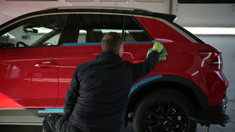 Ein Mann reinigt einen roten SUV mit einem Tuch in einer Werkstatt.