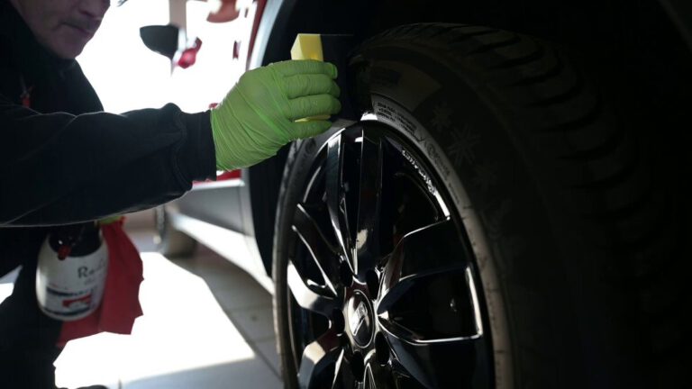 Person mit grünen Handschuhen reinigt einen Autoreifen mit einem Schwamm.